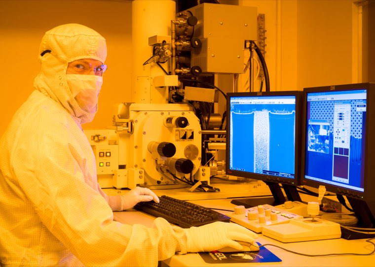 A researcher at a scanning electron microscope, reading results on two screens