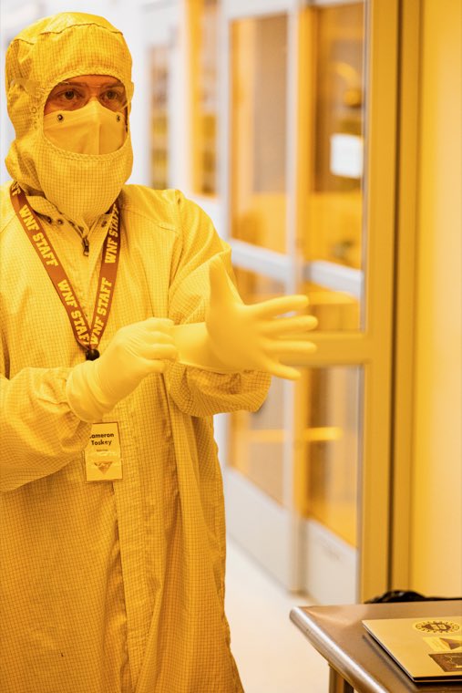 A researcher fully gowned in a cleanroom suit, hood, mask and gloves