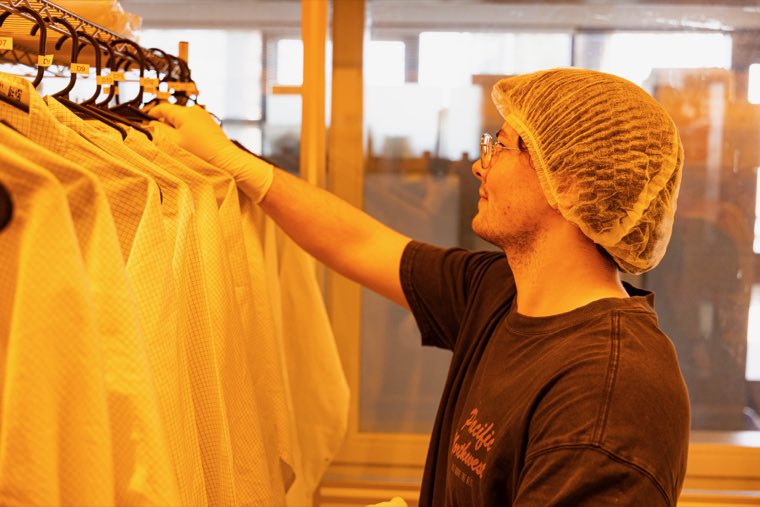 A researcher taking a cleanroom suit from a rack of them